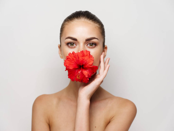 mooie vrouw rode bloem bijgesneden uitzicht kale schouders heldere huid - Foto, afbeelding