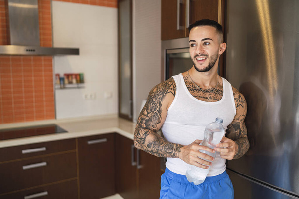A hot tattoed man drinking water in the kitchen - Foto, afbeelding