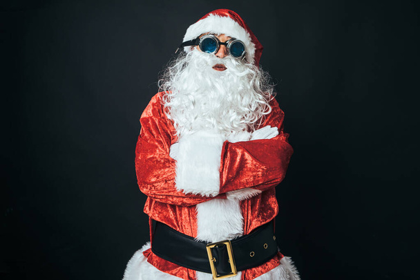 Man dressed as Santa Claus with Victorian style welder goggles, on black background. Concept of Christmas, Santa Claus, gifts, celebration. - Photo, Image