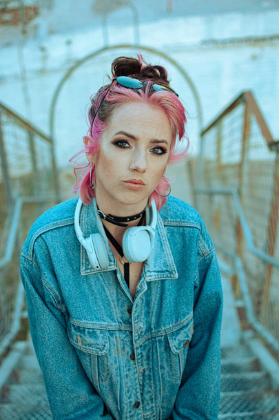 A vertical shot of a cool white lady with pink hair, headphones, gothic style makeup and clothing - Photo, image
