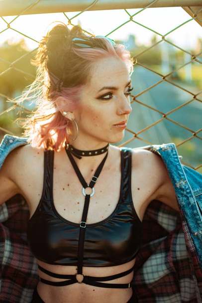 A vertical shot of a cool young Caucasian lady with pink hair, gothic style makeup and clothing - 写真・画像