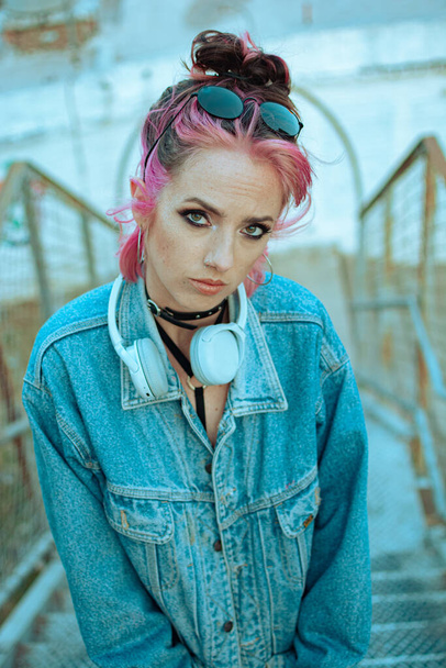 A vertical shot of a cool white lady with pink hair, headphones, gothic style makeup and clothing - Фото, изображение