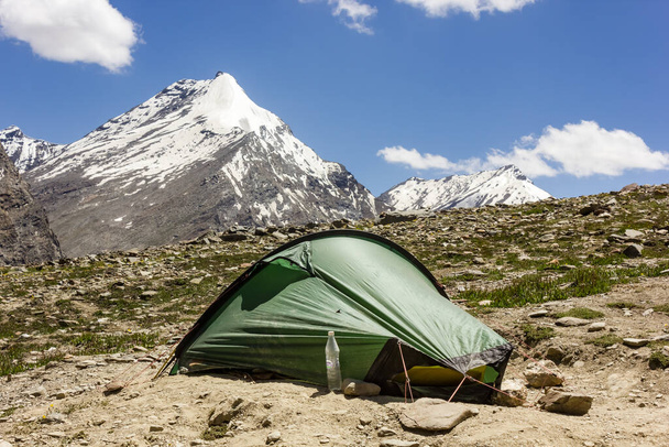 ZANSKAR, INDIA - Oct 10, 2021: Zanskar, India - July 2012: A green tent pitched on the rocky slope of a hill side with a view of snow capped Himalayan mountain peaks. - Foto, afbeelding