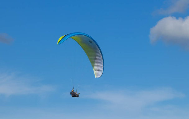A male paragliding against a cloudy blue sky - Foto, afbeelding