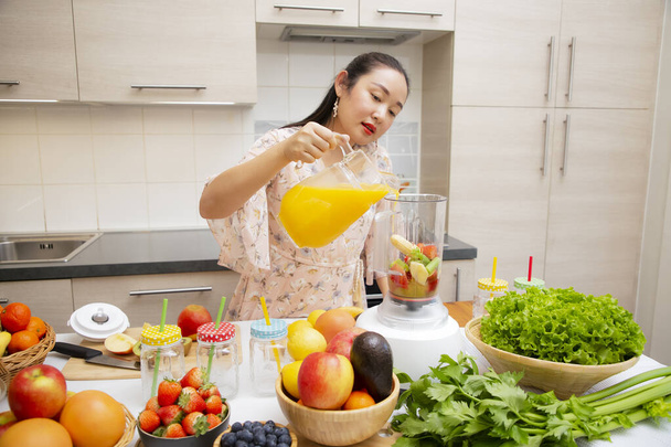 Mutlu kadın taze sıkılmış meyve ve sebze hazırlarken mutfakta kahvaltıda meyve püresi yapmayı seviyor. Diyet ve sağlık konsepti.. - Fotoğraf, Görsel