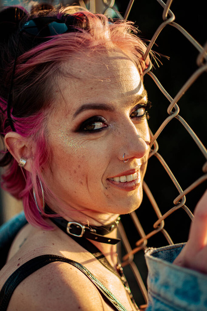 A vertical shot of a cheerful young Caucasian lady with pink hair, gothic style makeup and clothing - 写真・画像