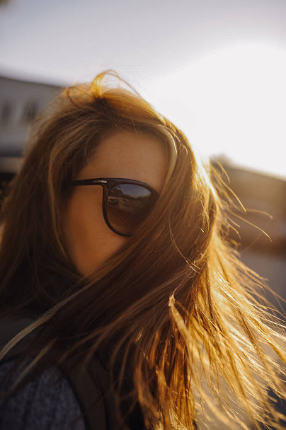 Portret młodej kobiety, jej włosy pięknie świecą w słońcu o zachodzie słońca, rozwija się i zakrywa twarz. stylowy wizerunek kobiety. ostrość pionowa, selektywna - Zdjęcie, obraz