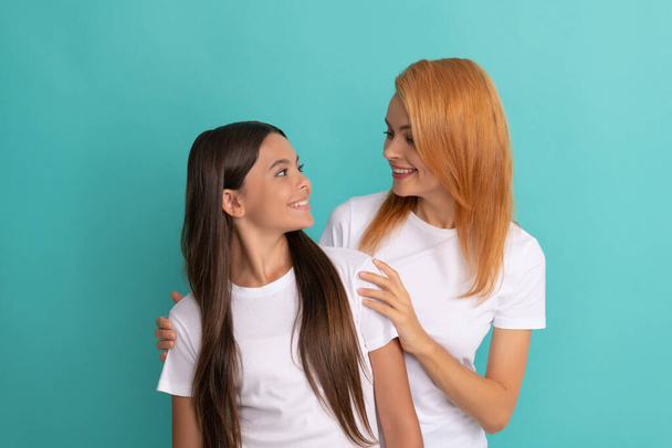 loving smiling woman hug daughter in white shirts on blue background, friendship - Photo, Image