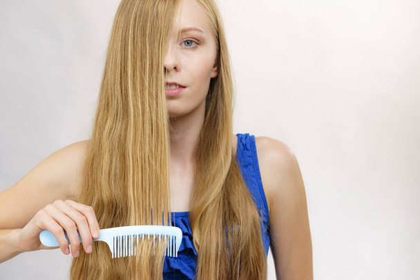 Young woman combing long healthy blonde hair, using comb - Фото, изображение