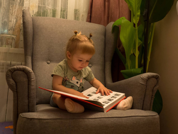 Egy kislány, aki egy könyvet lapoz, miközben székben ül, életstílusban. - Fotó, kép