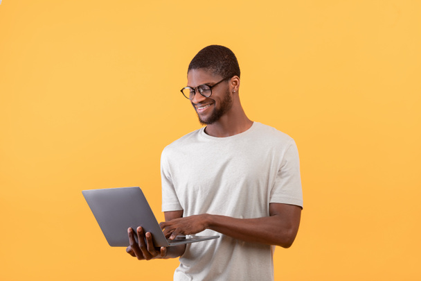 Freelance career. Positive african american guy using laptop and smiling, standing over yellow background - Φωτογραφία, εικόνα