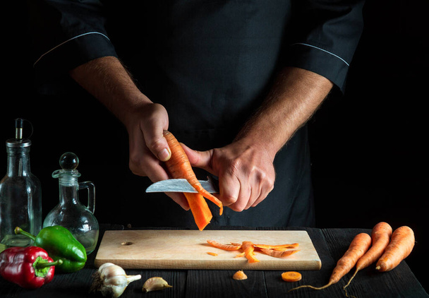 O chef profissional descasca cenouras para sopa de legumes em uma cozinha de restaurante. Close-up - mãos do cozinheiro durante o trabalho. Dieta de cenoura - Foto, Imagem