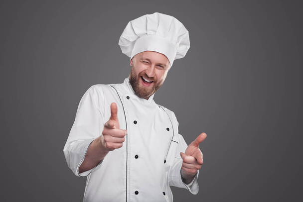 Cheerful chef pointing at camera and winking - 写真・画像