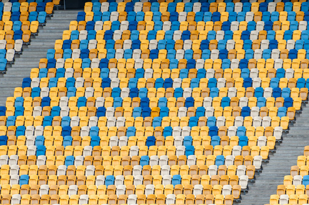 Blurred sitting fans colored plastic chairs at the football stadium background. Closeup of yellow and blue seats on stadium. ArenaLviv Ukraine. - Фото, зображення
