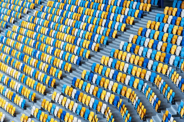 Blurred sitting fans colored plastic chairs at the football stadium background. Closeup of yellow and blue seats on stadium. ArenaLviv Ukraine. - Photo, Image