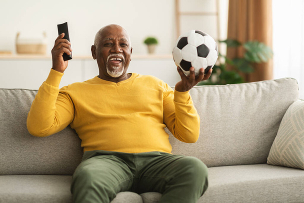 Старший африканский мужчина смотрит спорт по телевизору, празднуя победу в помещении - Фото, изображение