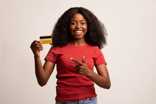 Alegre hembra negra señalando la tarjeta de crédito en su mano - Foto, Imagen