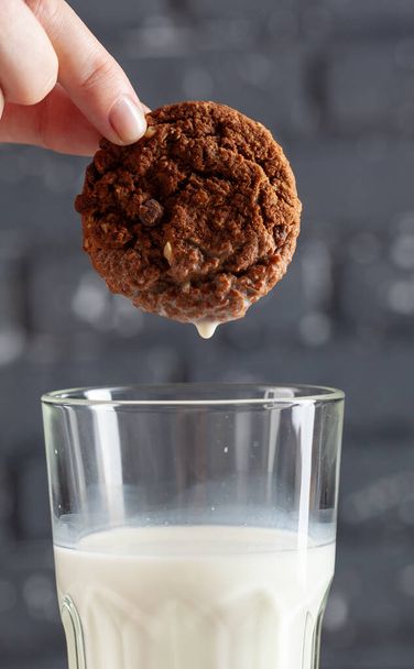 Female hand dunking cookie in milk close up - Фото, изображение