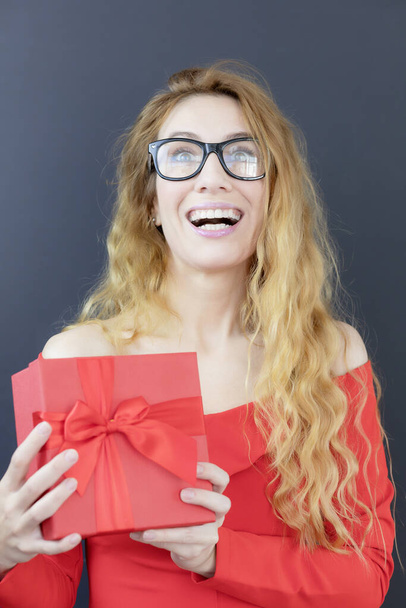 Chica rubia feliz con un regalo. La alegría de recibir un regalo. Dama de rojo con una caja de regalo. Cartel de vacaciones - Foto, Imagen