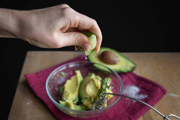 Egy nő guacamole-t készít egy érett avokádóval, ami lime-ot tör. Természetes egészséges élelmiszer. - Fotó, kép