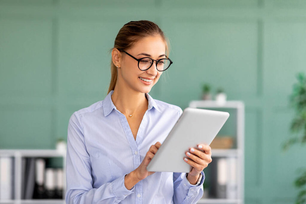 Glückliche Geschäftsfrau nutzt digitales Tablet an ihrem Arbeitsplatz im Bürobereich, liest Dokumente online, checkt E-Mails - Foto, Bild