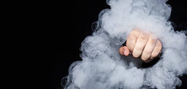 Чоловічий кулак всередині сигаретного диму на чорному тлі
 - Фото, зображення
