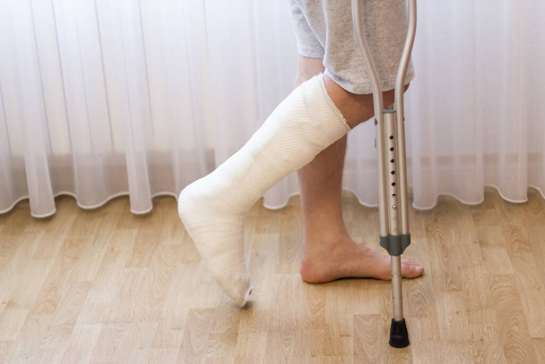 Close-up of man leg in plaster cast using crutches while walking. - Zdjęcie, obraz