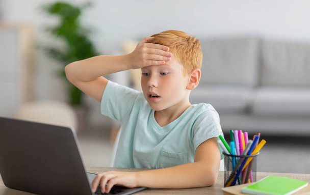 Schooler sitting in front of laptop, touching his forehead - Φωτογραφία, εικόνα