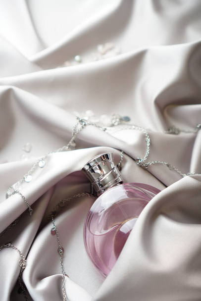 Pink women's perfume bottle in satin cloth draperies. Vertical photography. - Fotografie, Obrázek