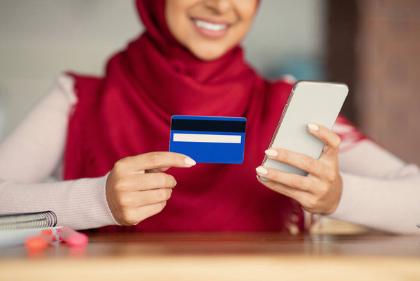 Señorita musulmana irreconocible usando teléfono móvil y tarjeta de crédito - Foto, imagen