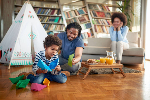 Glückliche Familie, die mit Papierbooten spielt und gleichzeitig die Zeit in entspannter Atmosphäre zu Hause zusammen verbringt. Familie, zusammen, Liebe, Spiel - Foto, Bild