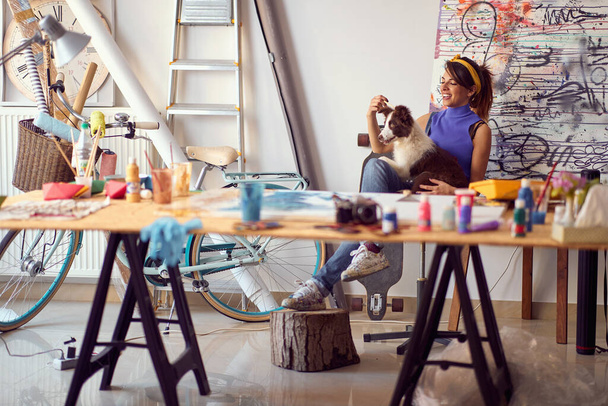 Smiling woman painter at workspace with her dog.Art, creativity and inspiration concept - Foto, imagen