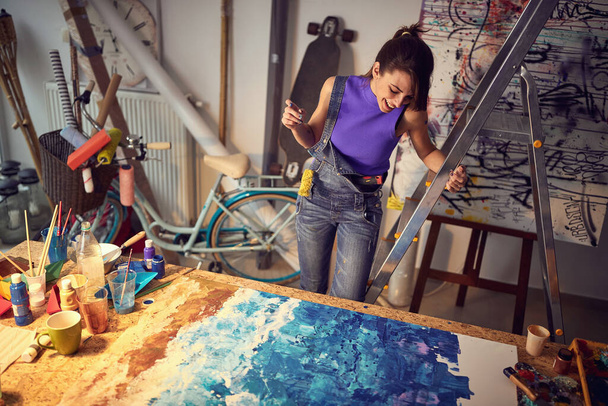 Smiling woman drawing on a camvas in art studio.Creative inspired mood. - 写真・画像