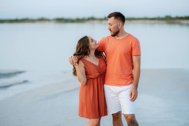 young couple in orange clothes with dog on an empty sandy beach - Фото, зображення