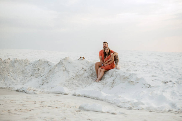 jeune couple en vêtements orange avec chien dans le désert sable blanc - Photo, image