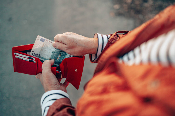Αγνώριστο θηλυκό βγάζει τραπεζογραμμάτια των 5 ευρώ από ένα κόκκινο δερμάτινο πορτοφόλι στο δρόμο. Καταβολή, μισθολογική και τραπεζική έννοια. - Φωτογραφία, εικόνα
