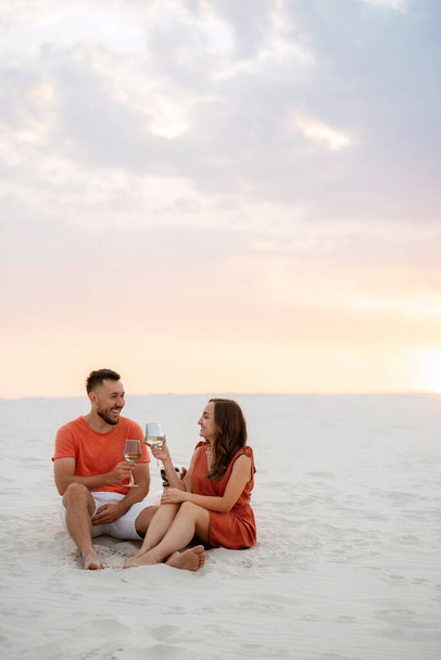 young couple in orange clothes with dog in the desert white sands - Фото, изображение
