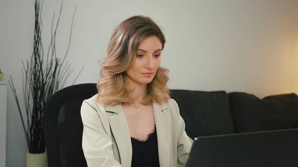 Close-up of pretty Caucasian business woman in gray suit working on laptop from home office. Concept confident woman and business woman, entrepreneur. - Photo, Image