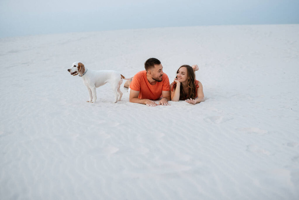 giovane coppia in abiti arancioni con cane nel deserto sabbie bianche - Foto, immagini