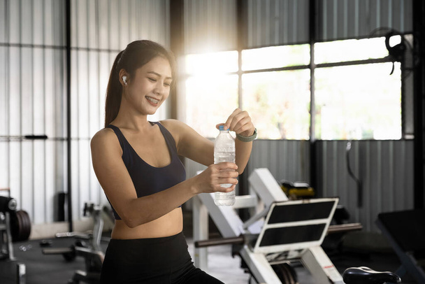 Asian young woman drinking water after workout in gym, healty and sport concept. - Фото, изображение