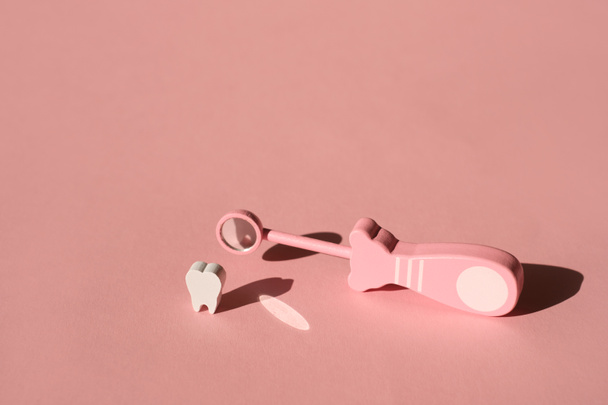 Speelgoed tandheelkundige inspectie spiegel voor het sluiten van tanden op roze achtergrond met diepe schaduw. Medisch Tandartsgereedschap. Concept van Tandheelkundige gezondheid. Reflectie van de tand in de spiegel. Houten speelgoed voor kinderen. - Foto, afbeelding