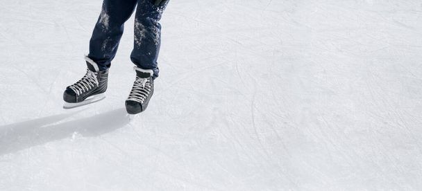 Ανδρικά πόδια σε παπούτσια πατινάζ στο παγοδρόμιο μια ηλιόλουστη χειμωνιάτικη παγωμένη μέρα. Πανοραμικό πανό με χώρο αντιγραφής για διαφημίσεις και προωθητικές ενέργειες για καλλιτεχνικό πατινάζ, σχολές χόκεϊ. - Φωτογραφία, εικόνα