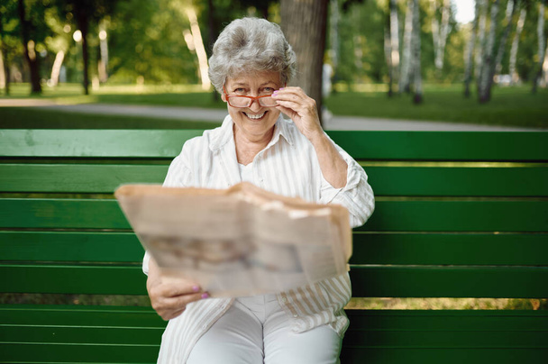 An elderly woman in glasses reading newspaper - Photo, Image