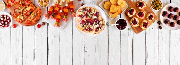 Winter holiday theme appetizers. Above view top border on a white wood banner background. Flatbreads, skewers, cranberry crostini and a mixture of party food. Copy space. - Photo, Image