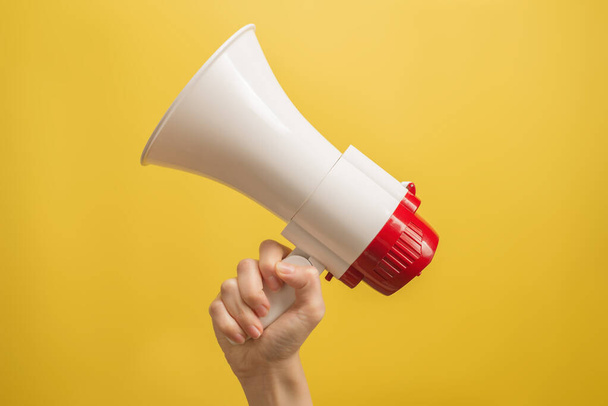 Megaphone in woman hands on a yellow background.  Copy space.  - Photo, Image