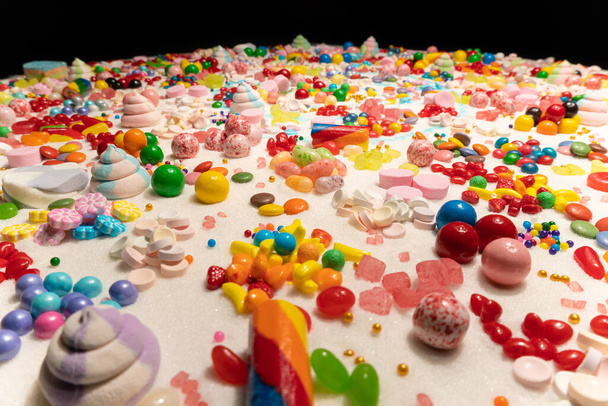 Candy in variety of colour, shape, size and flavours mixed on the table with real white sugar. International Candy Day background. Sweet stock of snack, chocolates, caramels, candy, and jelly beans. - Fotó, kép
