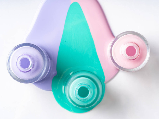 Pastel color spilled nail polish bottles over white - Foto, imagen