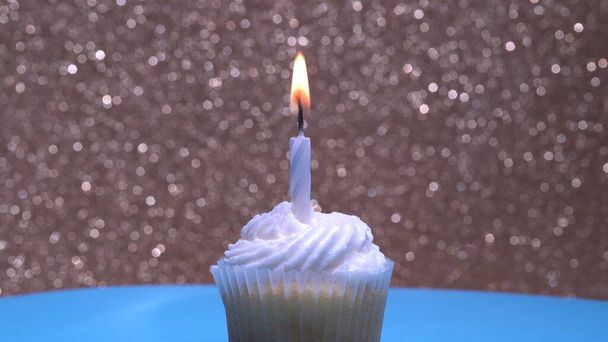 Cupcake with single birthday candle burning and sugar sprinkles icing on gold background. Delicious muffin decoration. Homemade vanilla cup cake with buttercream frosting. Shallow depth of field. - Foto, afbeelding
