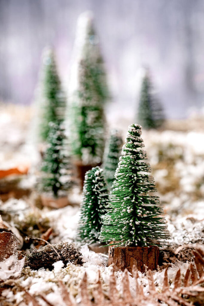 Christmas or New Year greeting card with decorative Christmas trees on snow covered moss with winter forest at background. Xmas holidays atmosphere - Foto, imagen