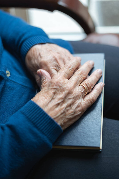 Las manos de una mujer mayor en un libro cerrado en una actitud de descanso y relajación. - Foto, imagen